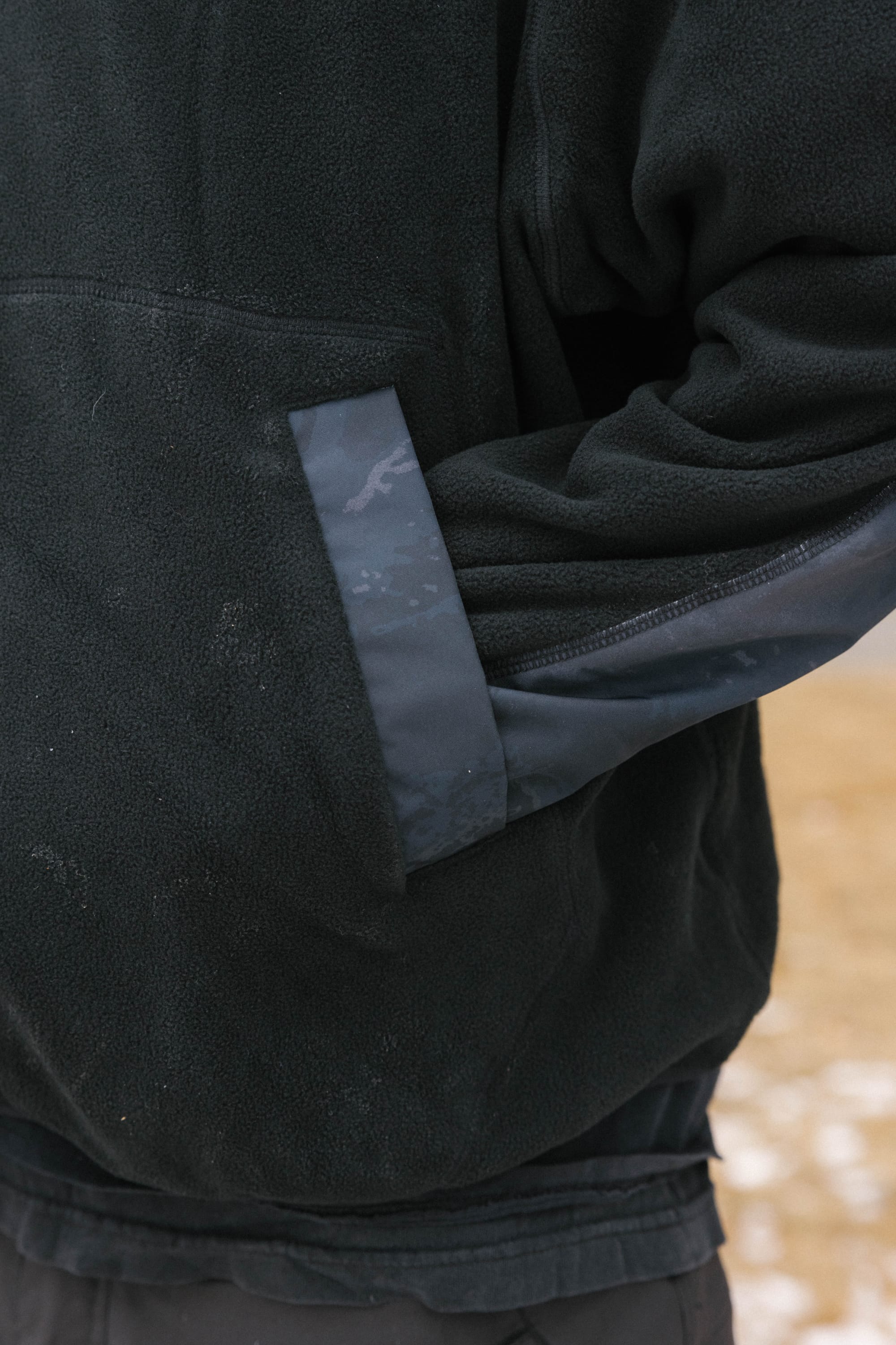 A person wearing the 686 Mens Clava Fleece Hoody stands outdoors on snowy ground with one hand in the side pocket. Only their torso and arm are visible.