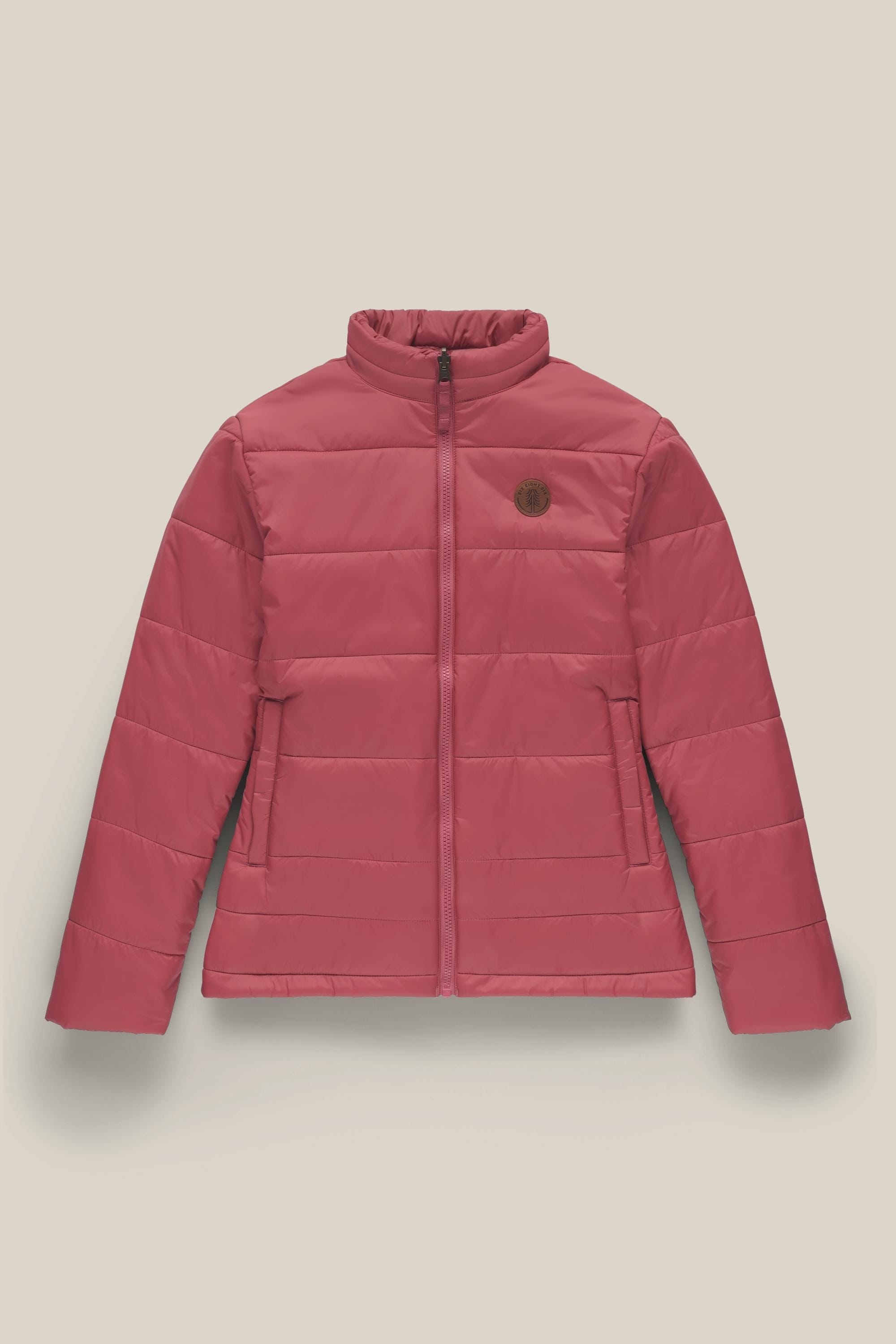 The 686 Womens Thermal Puff Insulated Jacket by 686 features a pink quilted design, high collar, front zipper, two side pockets, a circular brown chest patch, and is made from soft polyester. Shown against a light beige background.