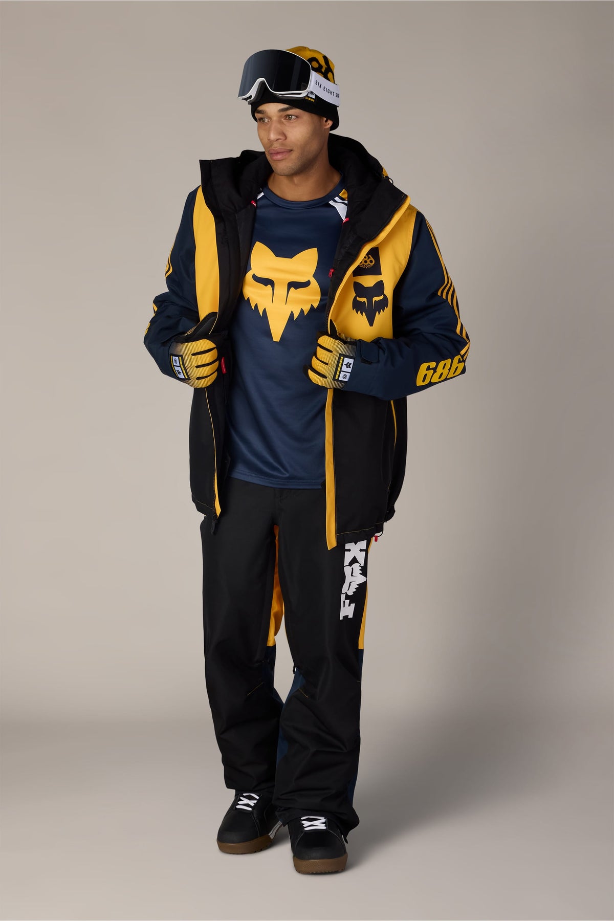 A man wearing a 686 Men’s Fox Racing Spec Insulated Jacket, pants, gloves, and snow goggles.
