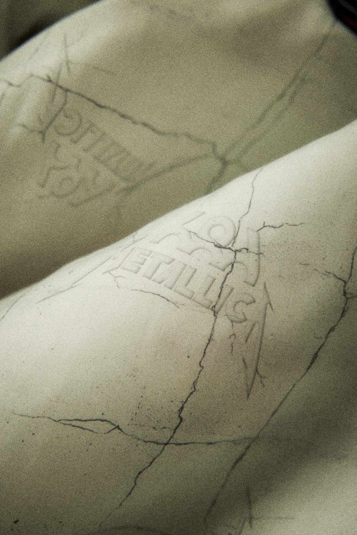 Close-up of a light-colored 686 Men’s Metallica One Insulated Jacket featuring a cracked texture and the Metallica logo embossed on the fabric.