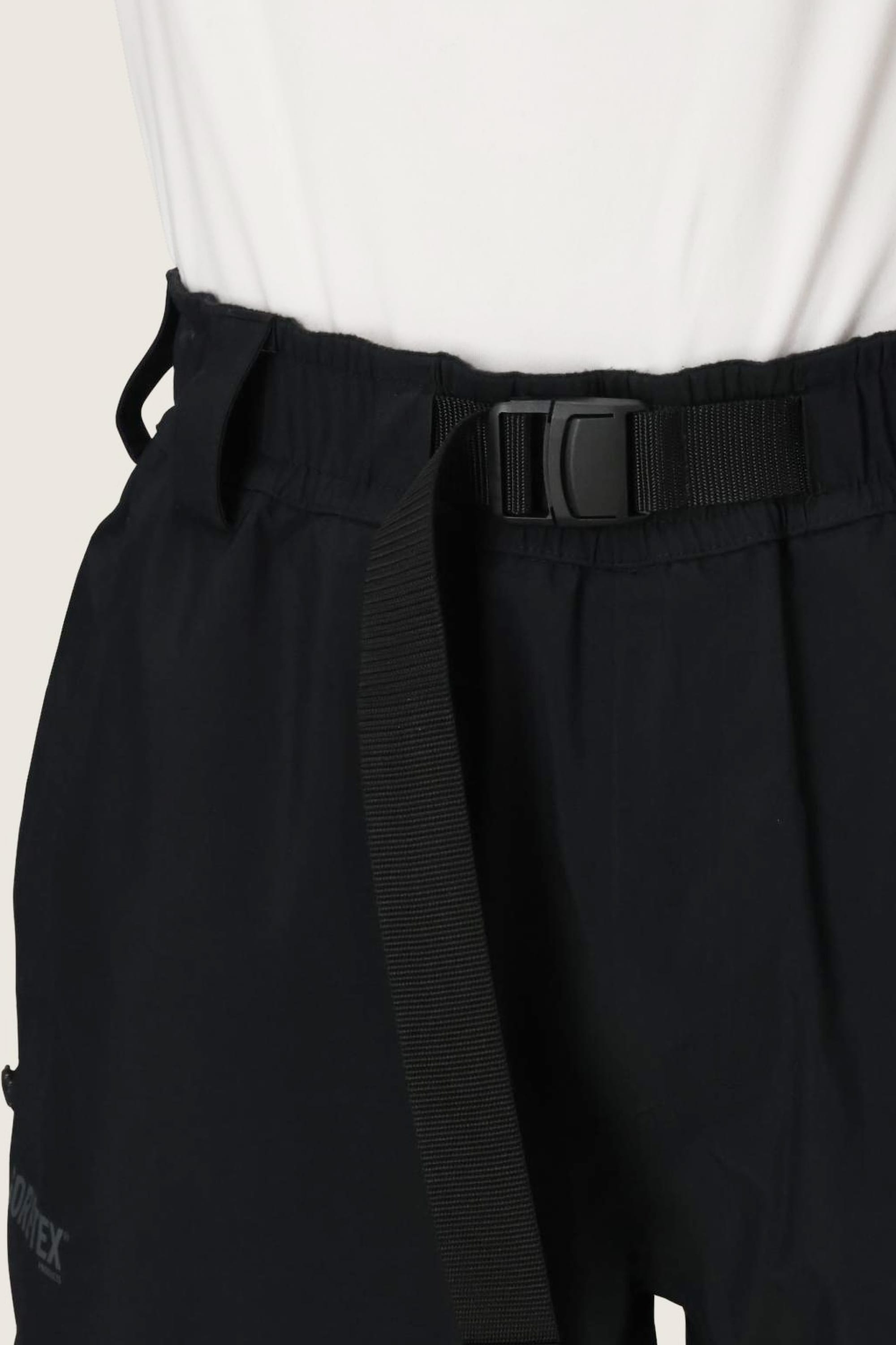 Close-up of a person wearing the 686 Men’s 686 Dojo® GORE-TEX® Shell Pant in black, featuring an adjustable belt with a plastic buckle, paired with a white shirt tucked in.