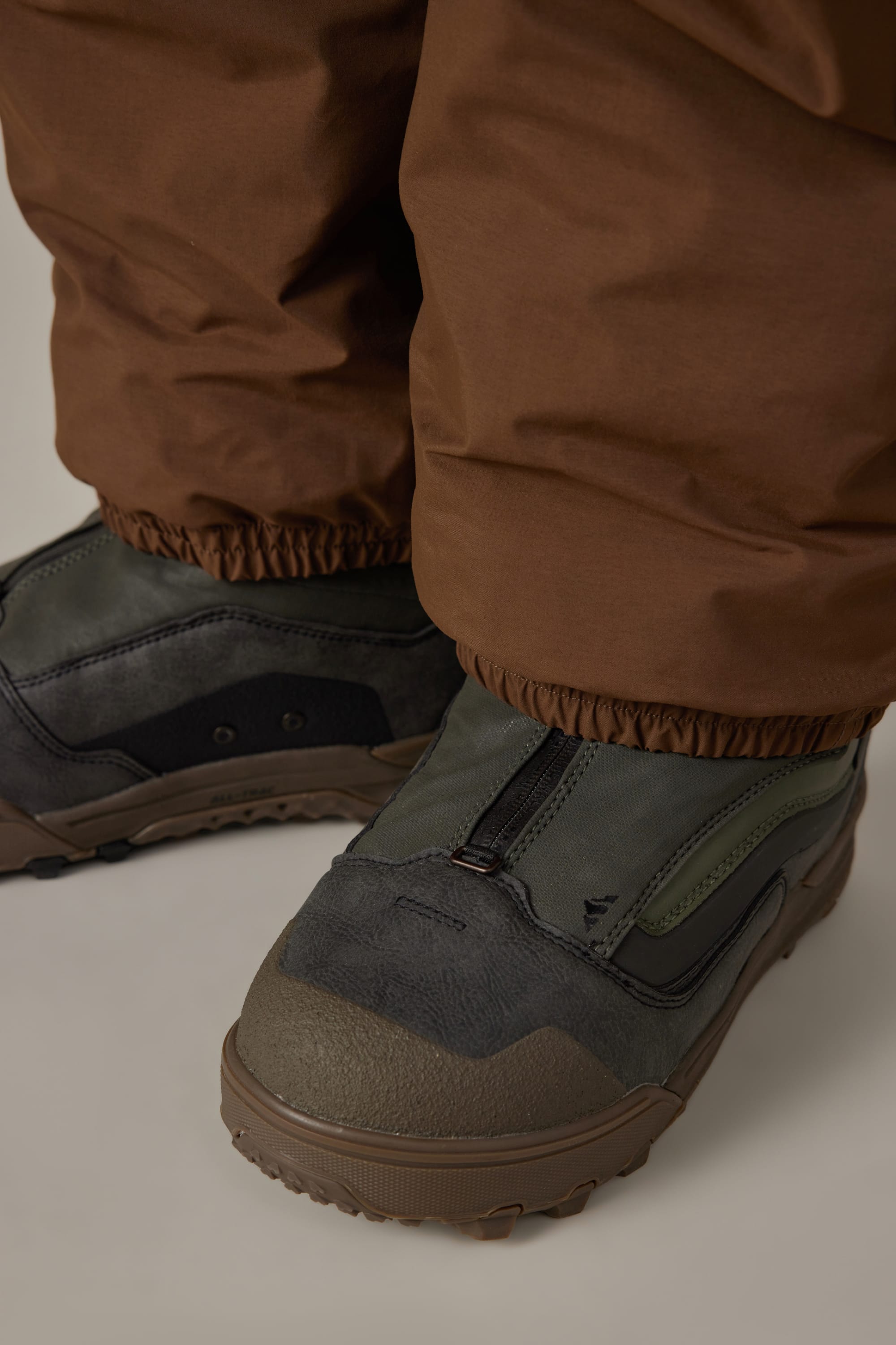 Close-up of a person wearing the 686 Men’s 686 Dojo® GORE-TEX® Shell Pant and green waterproof boots with black details and zipper closures.