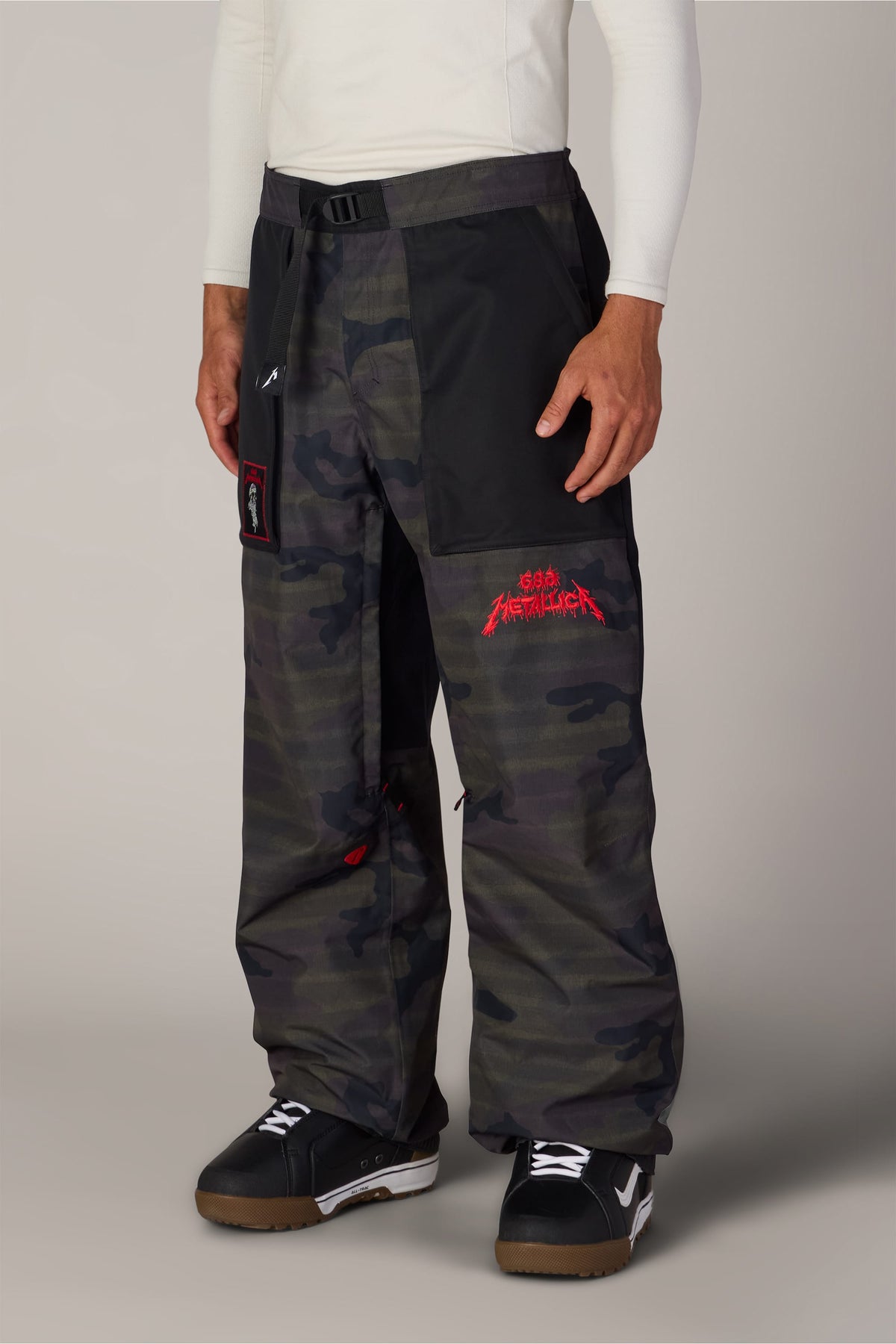 686 Men’s Metallica One Shell Pant in dark camo print with a black waistband, integrated belt, and red Metallica logo embroidery on the left thigh.