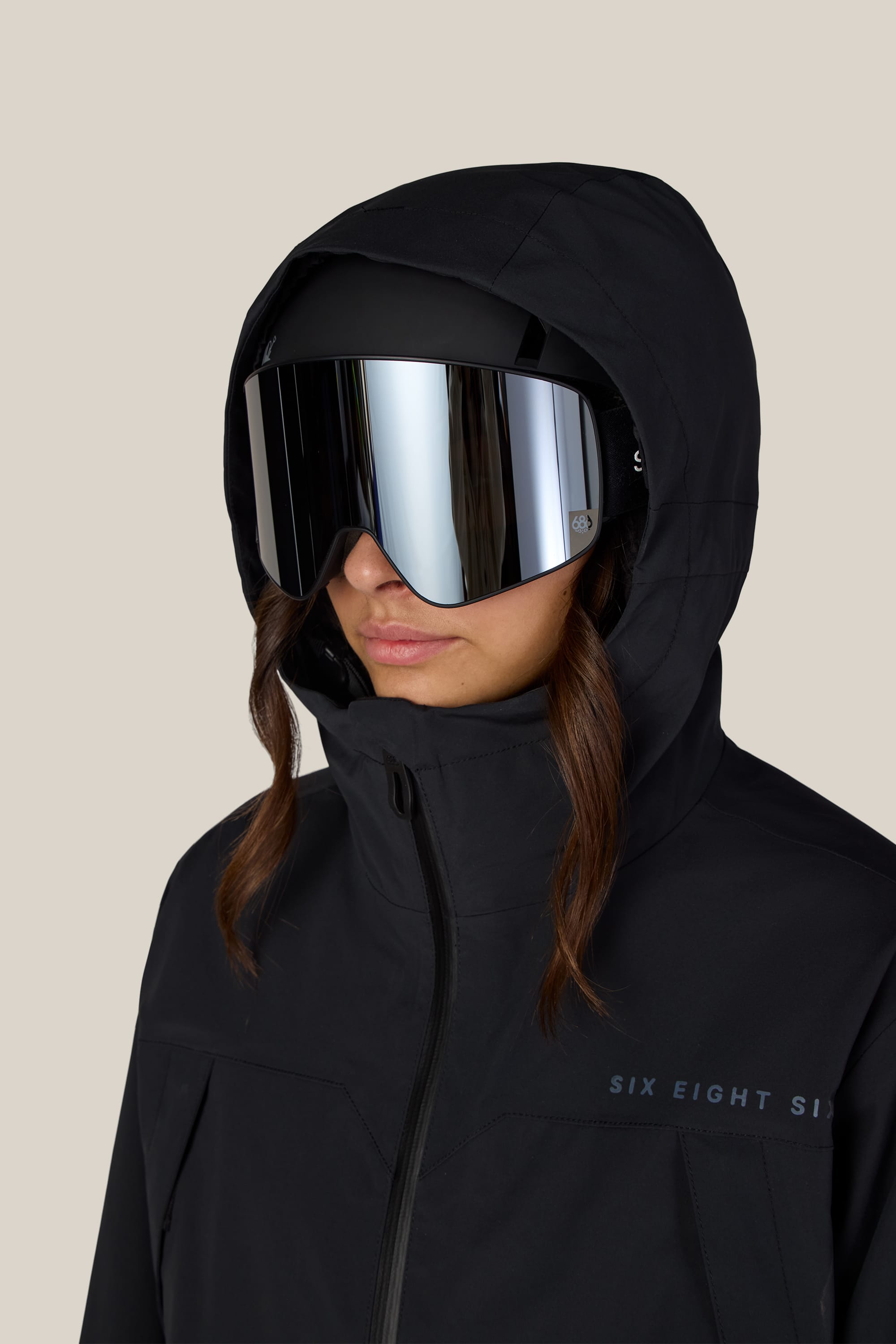 A person wearing the 686 Women’s SMARTY® 3-in-1 Framework™ 3L Jacket in black with a hood and large reflective ski goggles, facing forward against a plain light background.