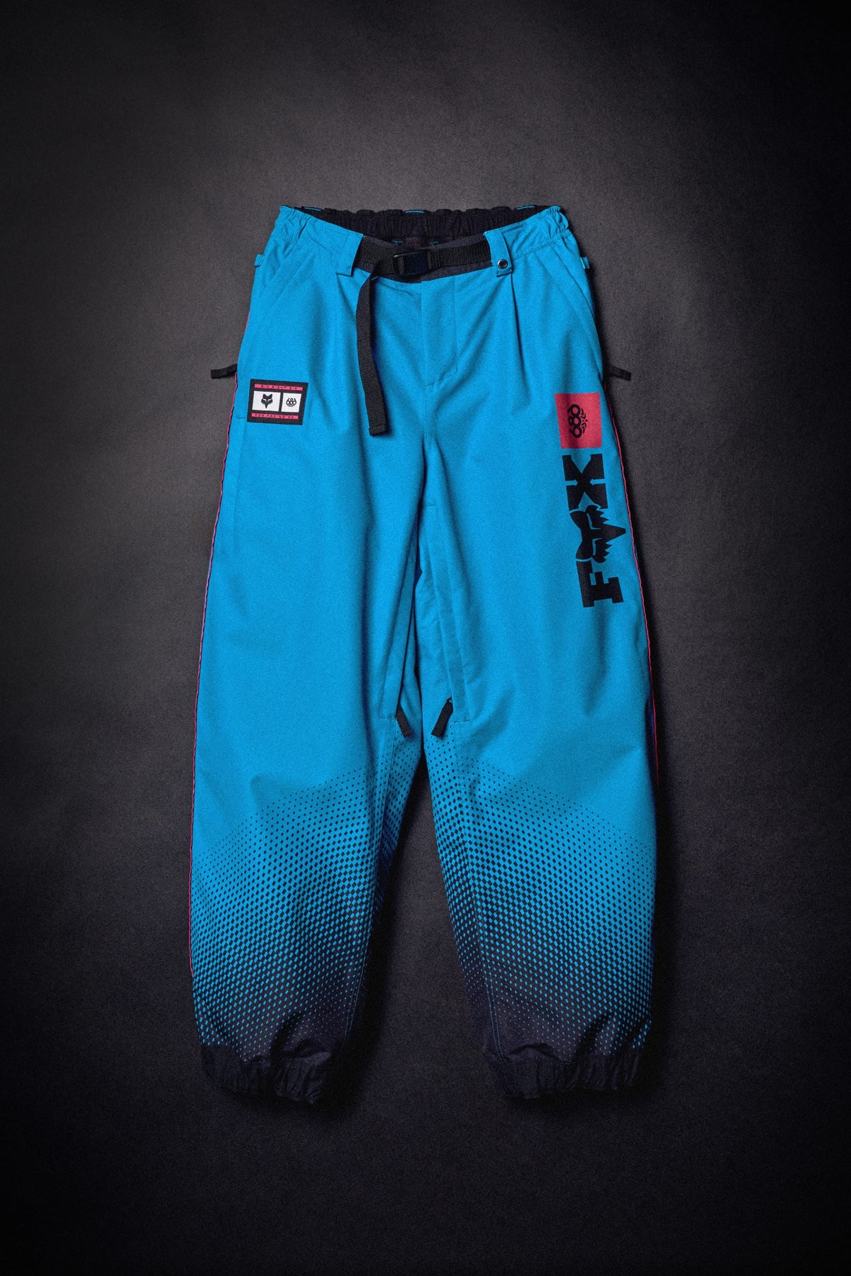 Bright blue 686 Women’s Fox Racing 97 Shell Pant with a black waist belt, a black and red patch, and vertical FOX branding on the left leg.