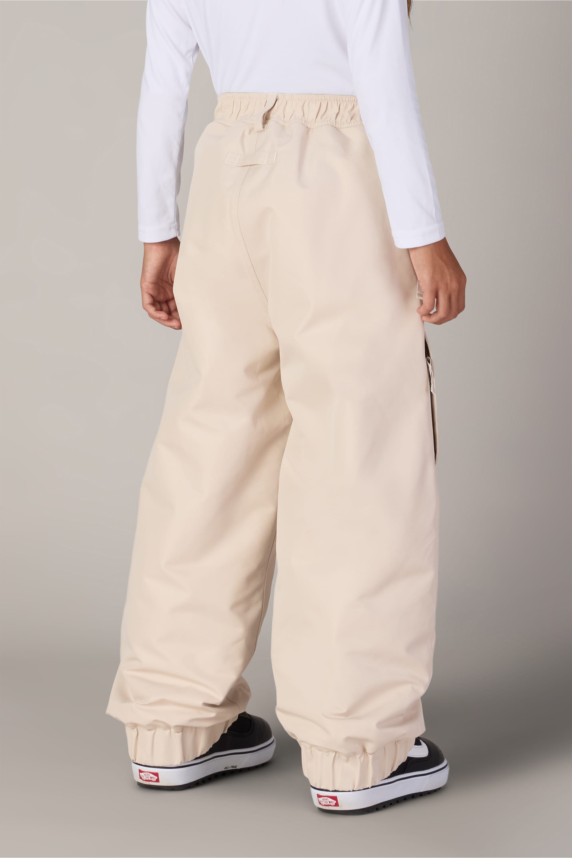 A person is shown from the back, standing against a neutral background, wearing the 686 Girls’ Outline™ Insulated Pant by 686—baggy woven pants in off-white with elastic cuffs—paired with a white long-sleeve shirt and black sneakers.