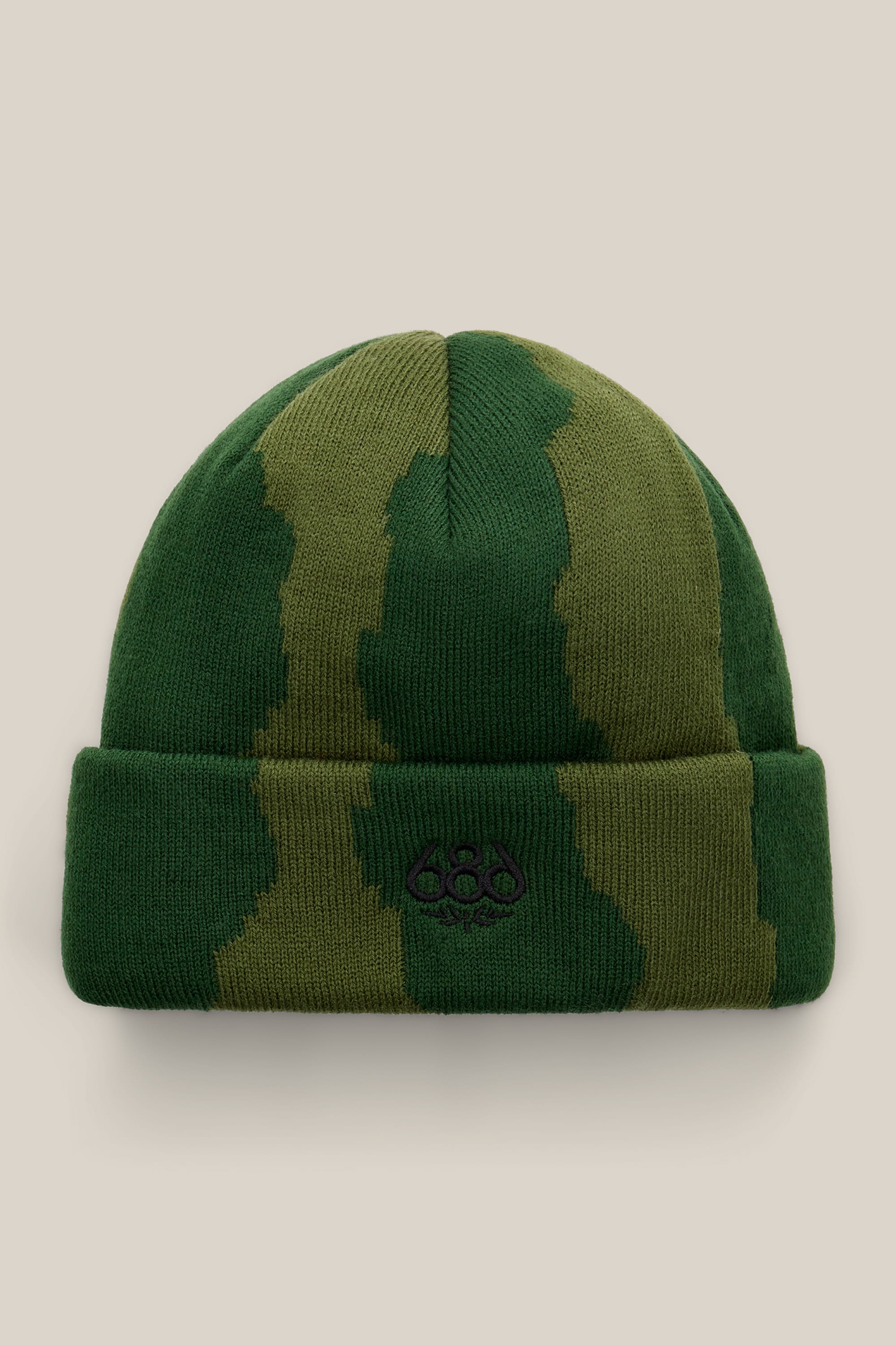 The 686 Torn Beanie by 686 features a green and olive camo-patterned acrylic knit with a folded brim and a small black embroidered logo on the front, set against a light beige background.