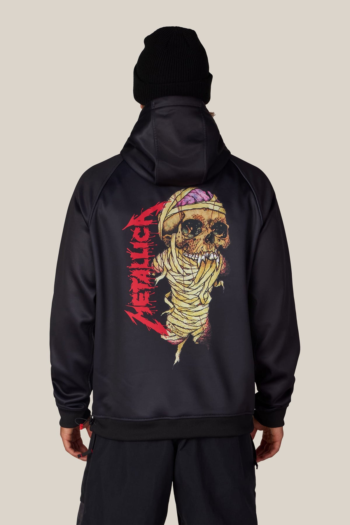 Back view of a person wearing a black 686 Men’s Metallica Bonded Fleece Pullover Hoody featuring a graphic of a bandaged skull and a red Metallica logo on the back.