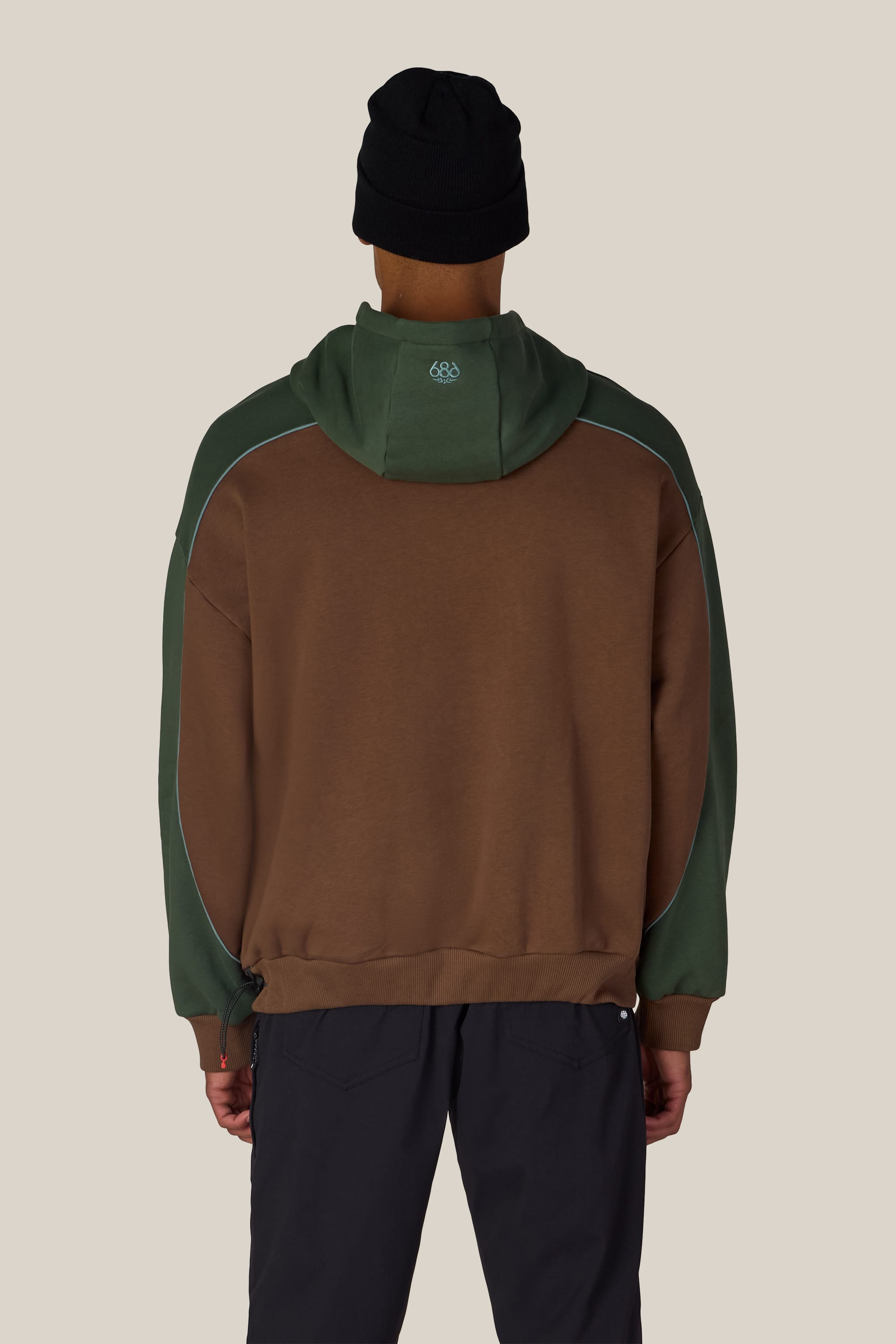 A person wearing the 686 Legacy Premium Heavyweight Hoody by 686, along with black pants and a black beanie, is shown standing with their back to the camera against a plain light background.
