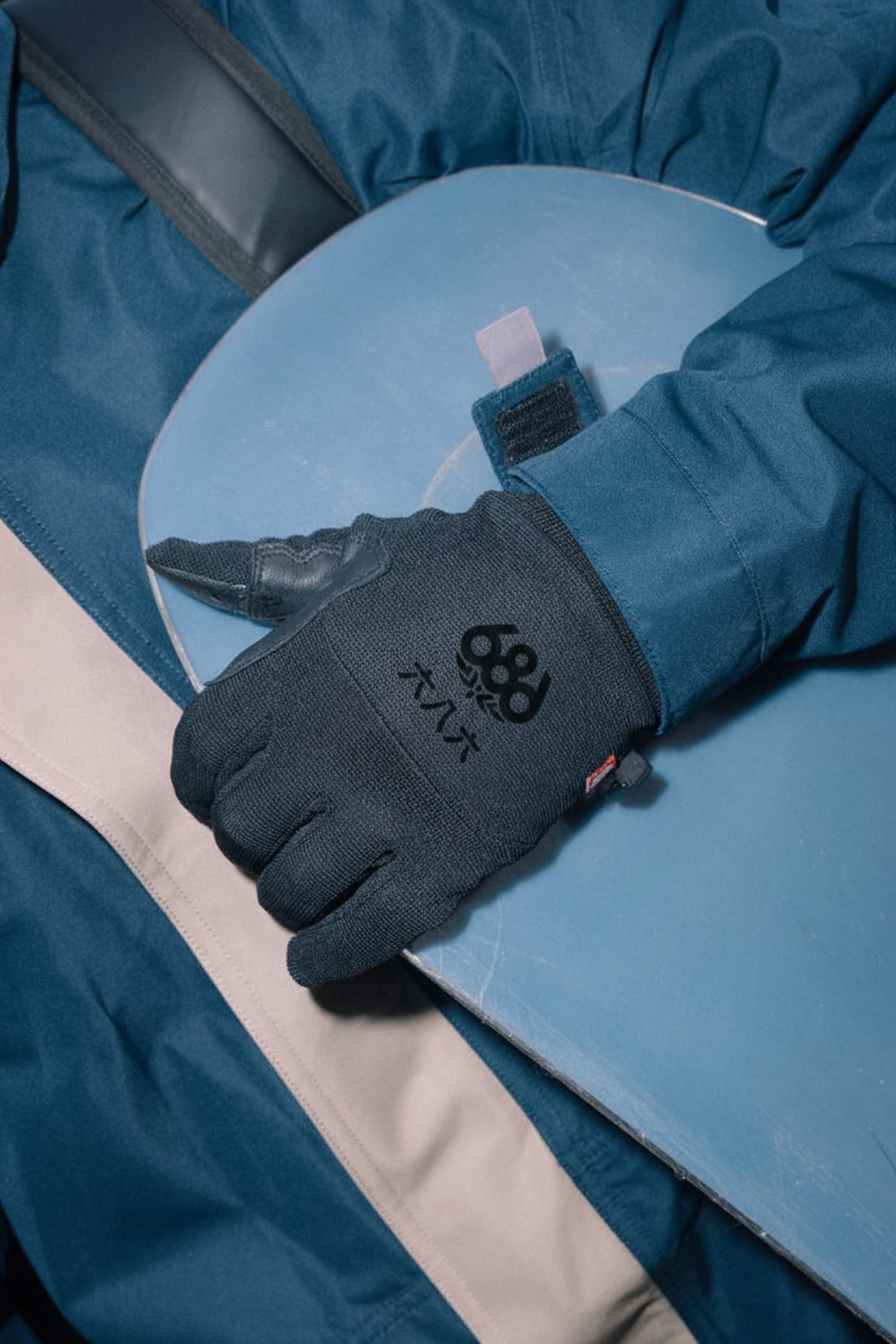 A person wearing a blue jacket and 686 Men’s Hold Up Pipe Glove holds a blue snowboard.
