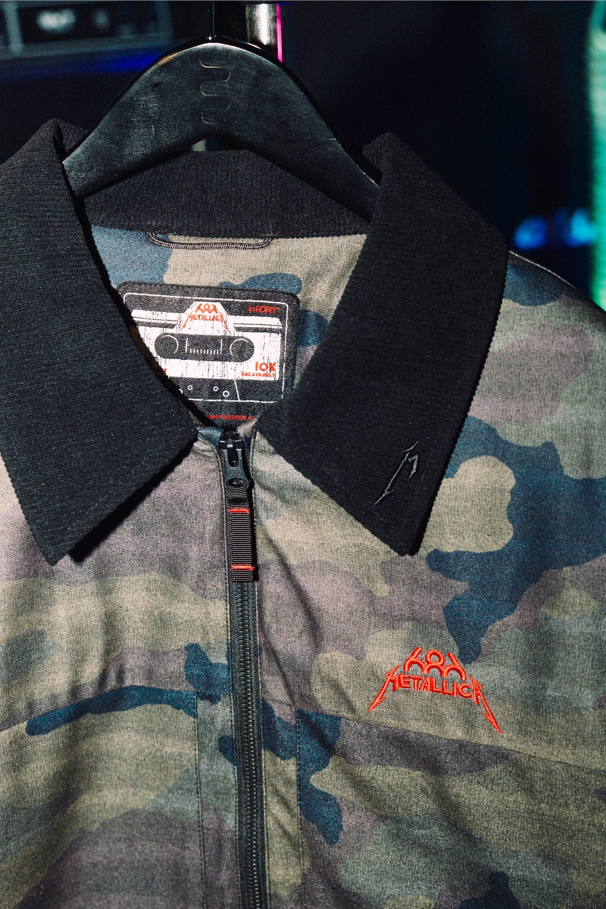 686 Men’s Metallica Caim Jacket in camo-print with a black collar and a red Metallica logo embroidered on the chest.