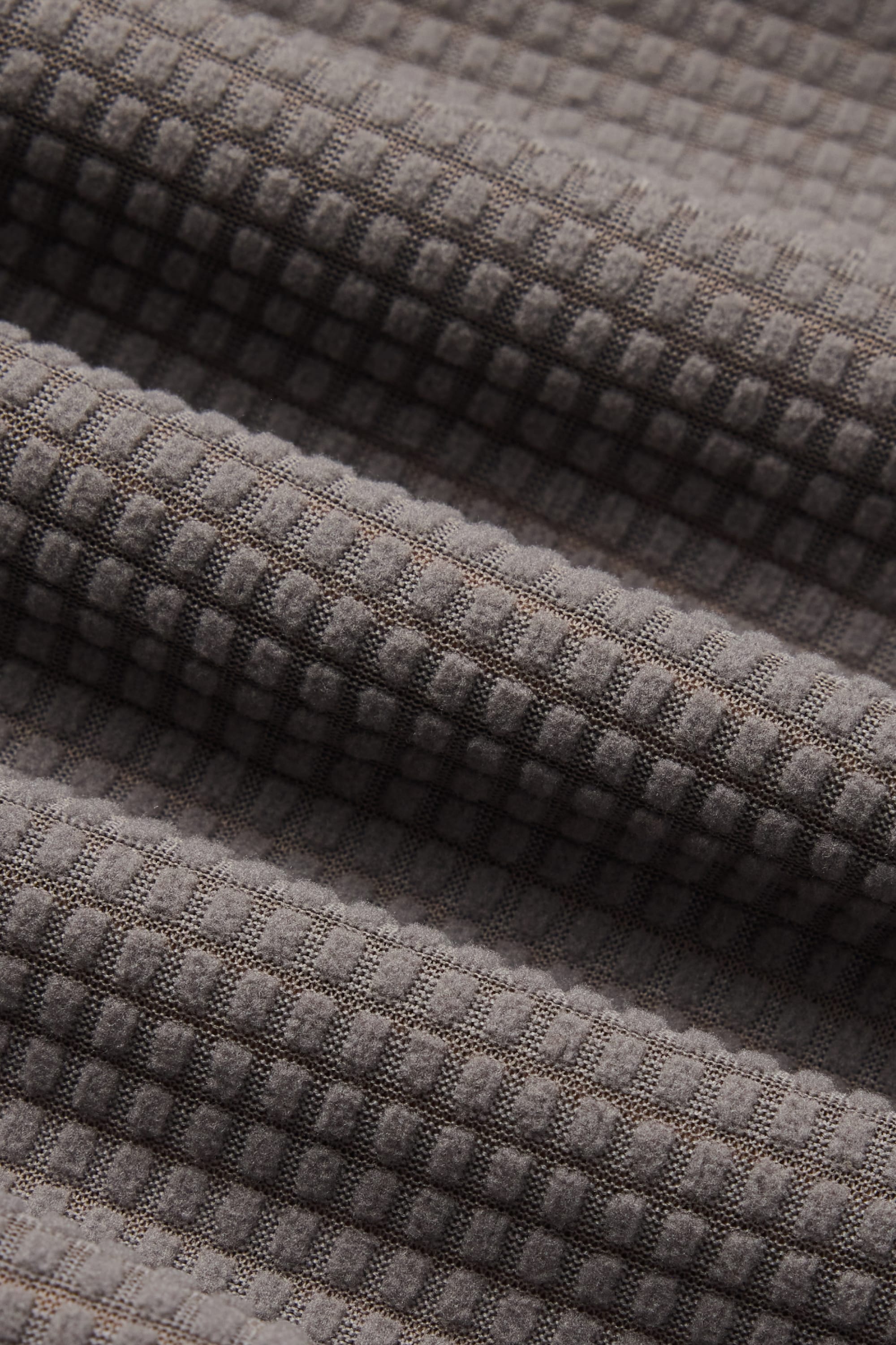 Close-up of the 686 Men’s Mission Grid™ Pant by 686, featuring gray fabric with a distinctive waffle or grid texture—raised squares and soft diagonal folds evoke the premium construction typical of men’s knitwear.