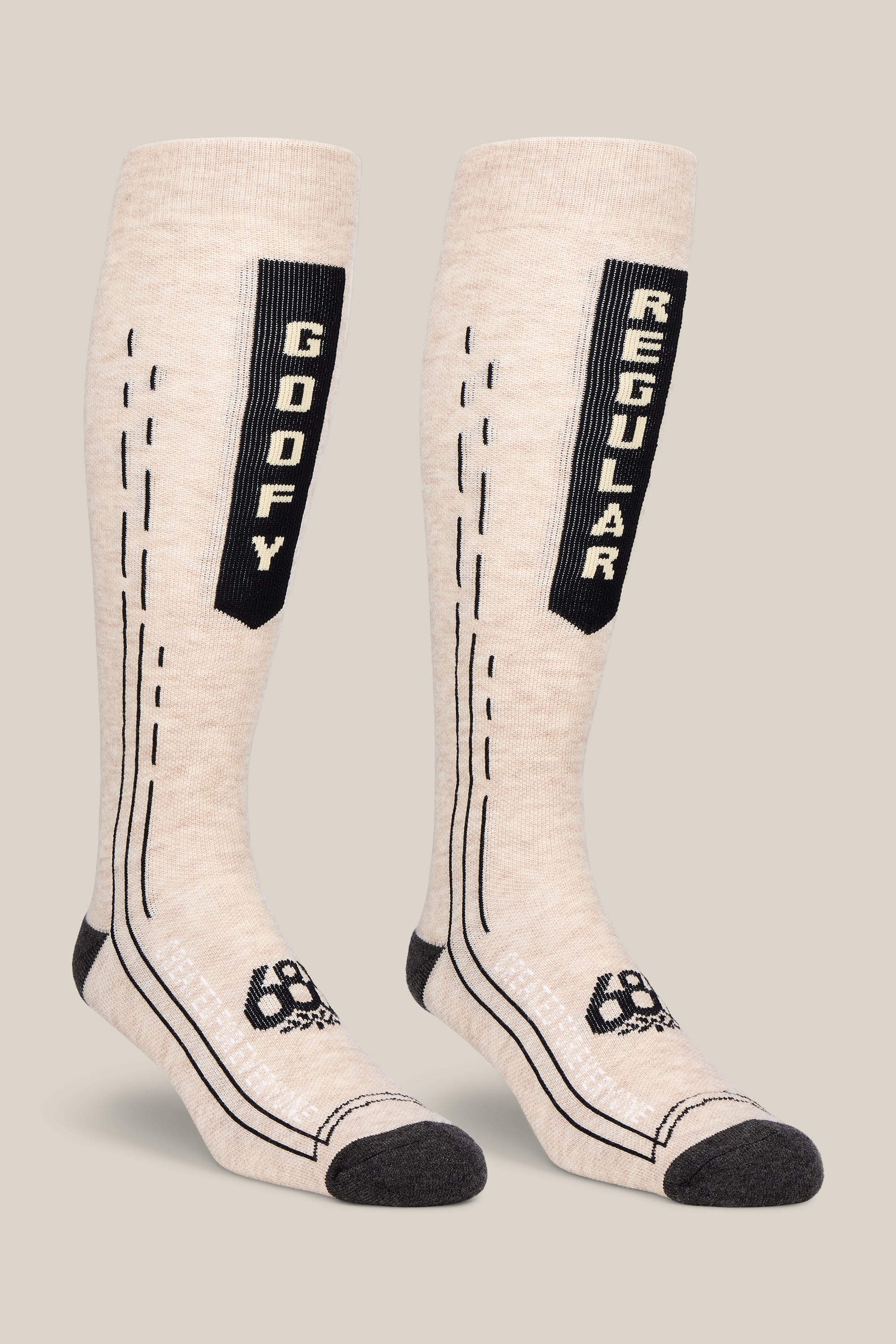 Here’s a revised version using your product data: The 686 Men’s Merino Balance Sock - 2-Pack from 686 includes a pair of tall, beige men’s performance socks with black toes and heels. One sock features “GOOFY” written vertically, while the other is labeled “REGULAR.” Both socks showcase stylish black stitched lines and a small logo near the toes for added detail.