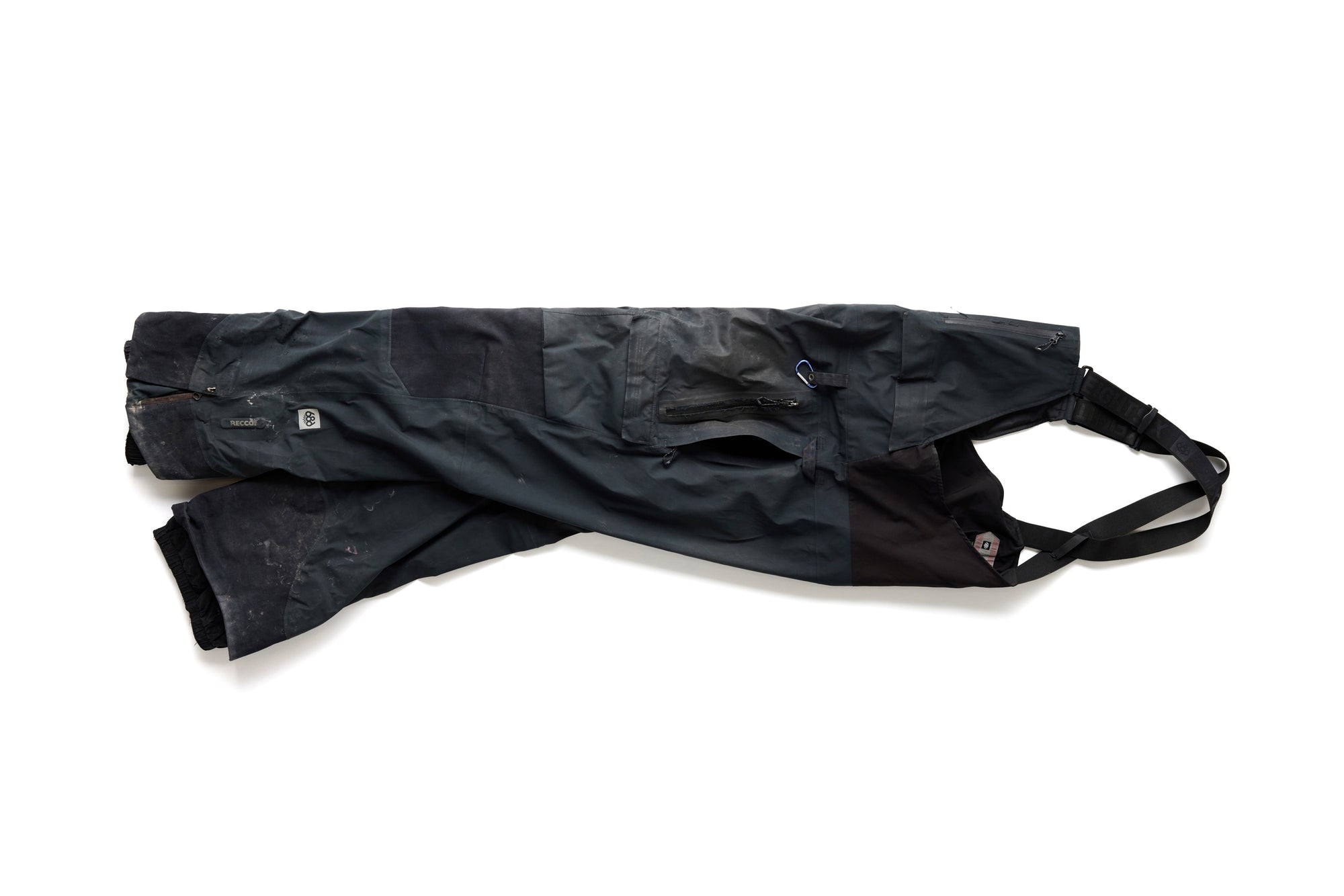 A pair of dark-colored, insulated snow pants with built-in suspenders, lying flat on a white background.