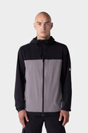 A man with a shaved head wears the 686 Mens ATP Stretch Wind Jacket by 686, featuring black sleeves and a gray front panel, standing against a light gray background.