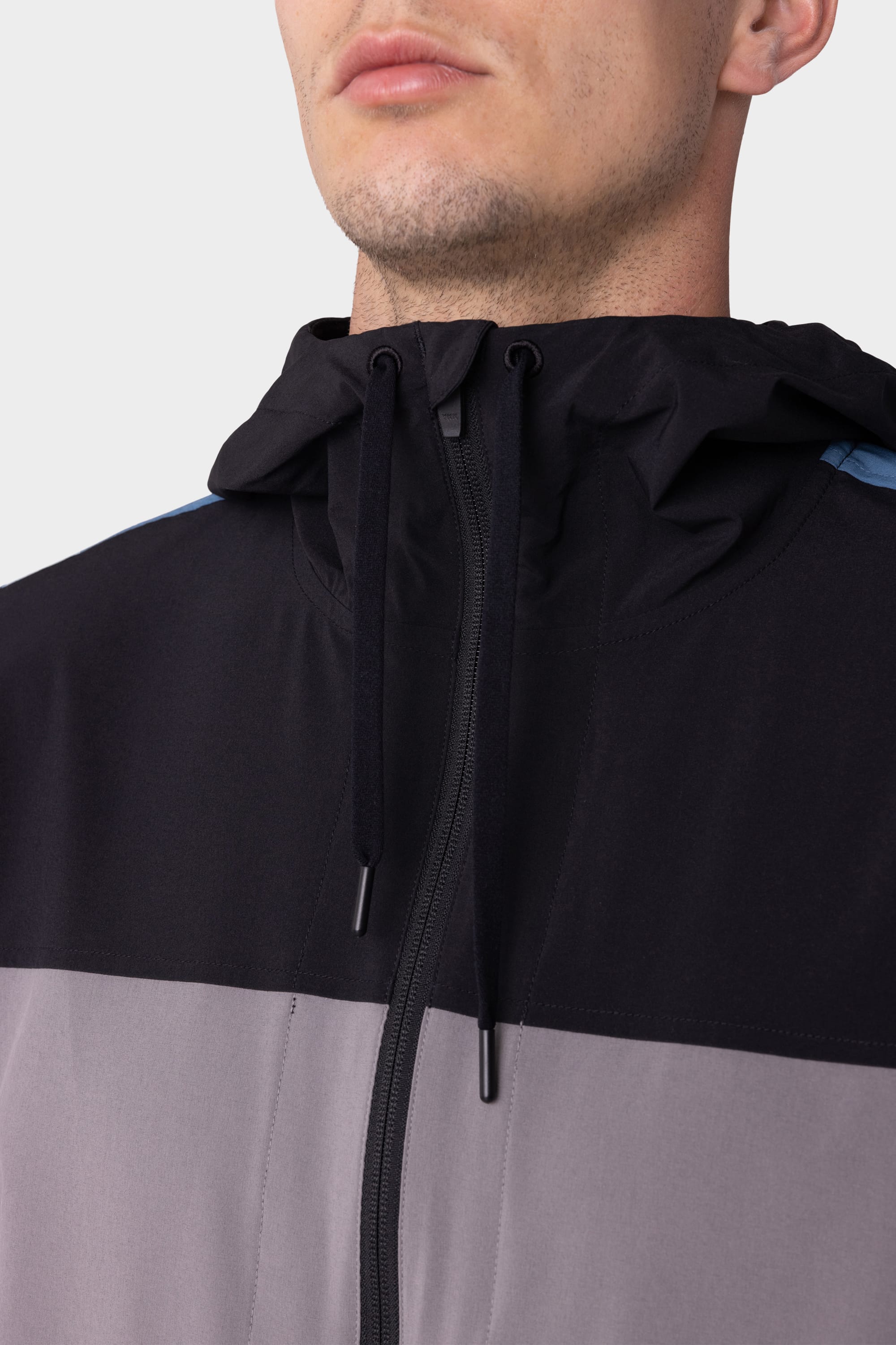 A close-up of a person wearing the 686 Mens ATP Stretch Wind Jacket, featuring black and gray color-blocking and a hood with black drawstrings. The persons face is partially visible from the nose down.